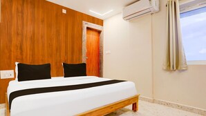 A hotel room with a bed, wooden panel walls, an air conditioning unit, a window with curtains, and a door. - Deluxe Sri Padmavati Ammavaari Temple Rama Grand (Tirupati)
