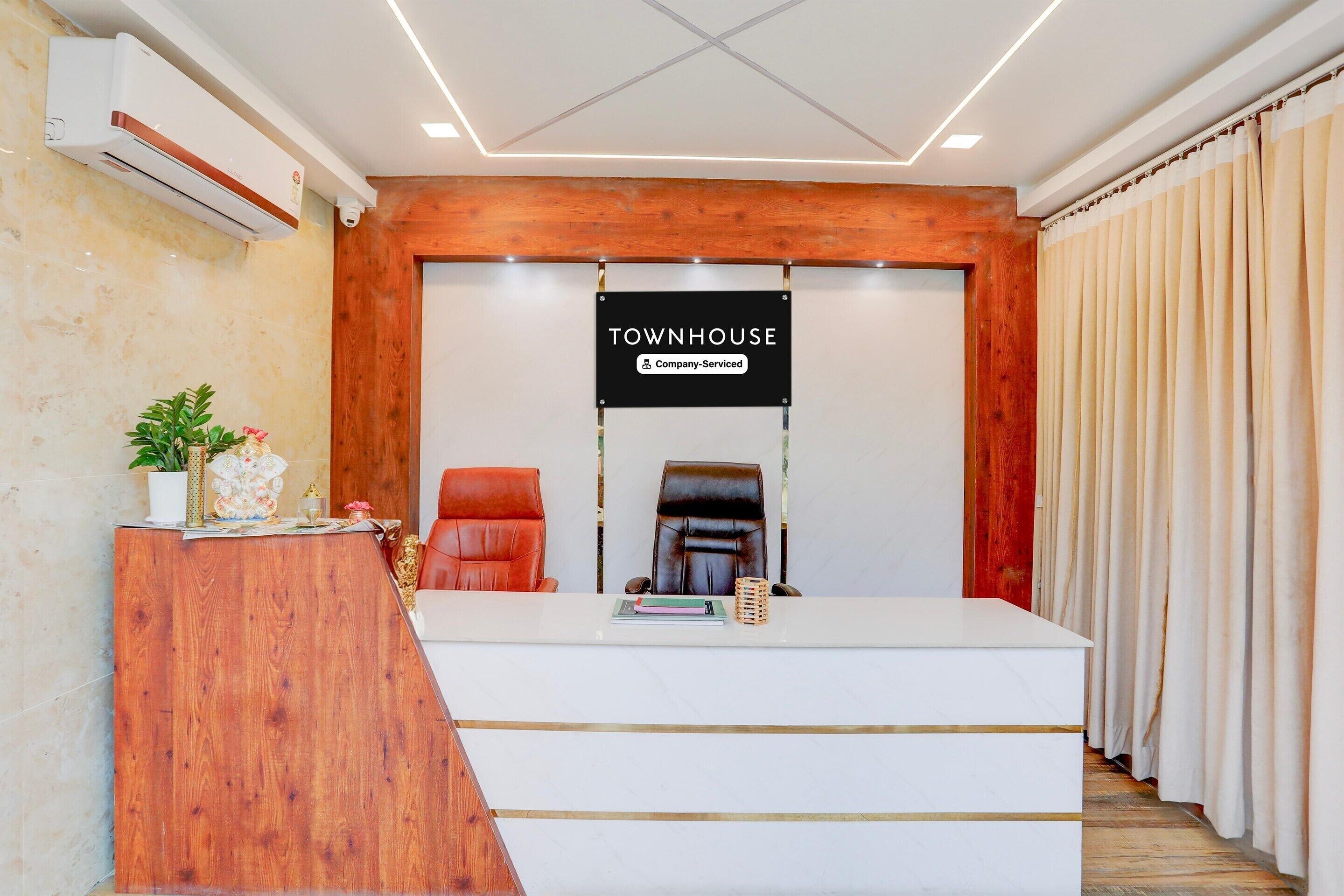 A reception area with a wooden desk, two leather chairs, a sign reading 'TOWNHOUSE Company Serviced', and a potted plant.