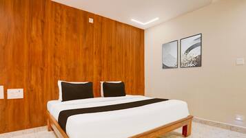 Un dormitorio con cabecera de madera, cama con ropa de cama blanca, dos almohadas negras y dos obras de arte enmarcadas en la pared.