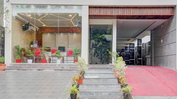 Una entrada moderna de edificio con fachada de vidrio, zona de estar al aire libre y una rampa que lleva a la entrada.