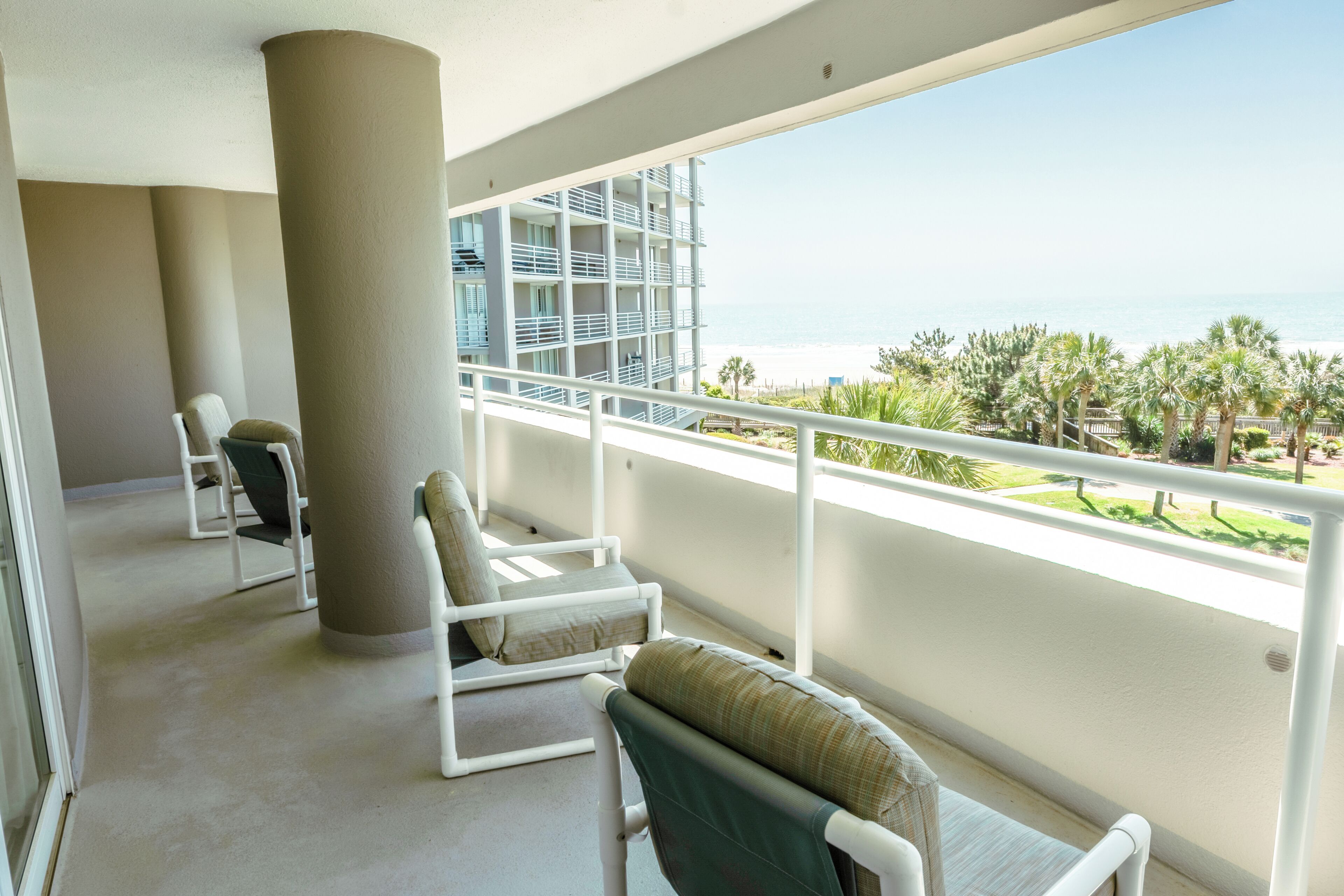 Un balcone con ringhiere bianche, due poltrone e vista su un edificio e una spiaggia.