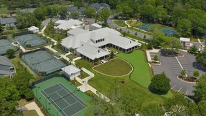 Luchtbeeld van een woongebied met meerdere tennisbanen, een groot gebouw met een plat dak en omliggend groen.