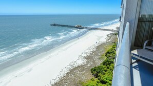 Uitzicht op het strand vanaf een balkon, met een pier die zich uitstrekt in de oceaan.