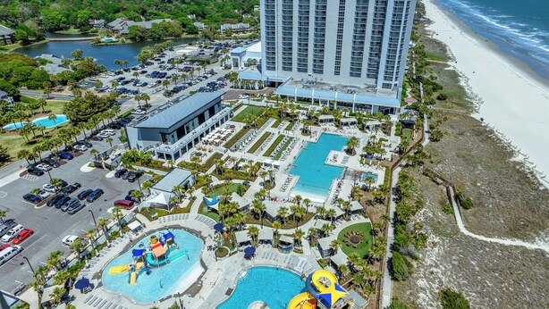 Een resort met meerdere zwembaden, een groot hotelgebouw en een strand.