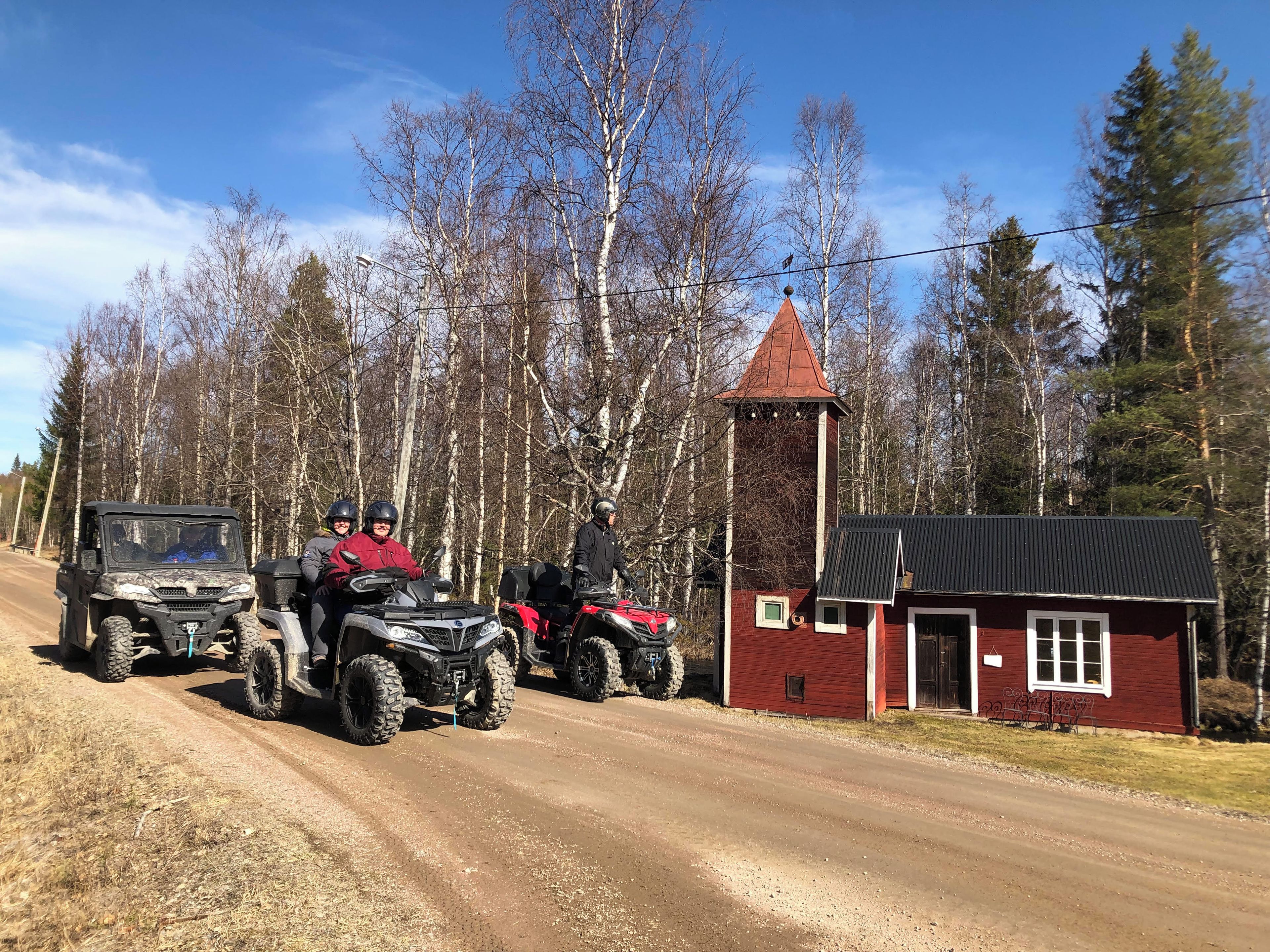 A dirt road with off-road vehicles and a red building with a tower.