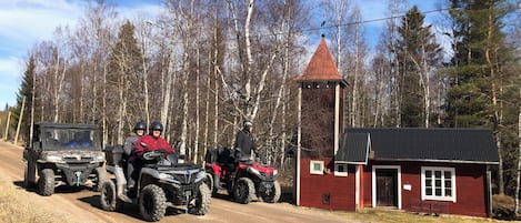 A dirt road with off-road vehicles and a red building with a tower.