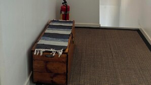 A loft bedroom with a sloped ceiling, a wooden chest, a patterned rug, a fire extinguisher, and a hanging lamp. -  The Old Farmhouse (Hammarstrand)