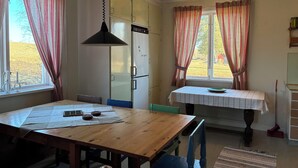 A dining area with a wooden table, chairs, a hanging light fixture, and a window with curtains. -  The Old Farmhouse (Hammarstrand)