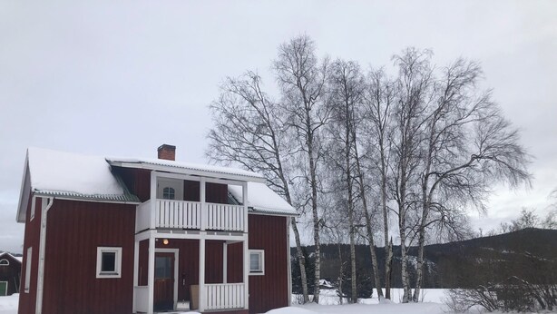 A two-story house with a balcony, surrounded by snow-covered ground and trees. -  The Old Farmhouse (Hammarstrand)