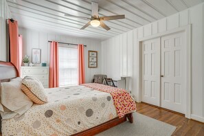 Ein Schlafzimmer mit Bett, Deckenventilator, Fenster mit Vorhängen, einer Tür und einem Nachttisch.
