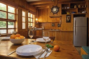 Ein Holzinterieur mit einem für zwei Personen gedeckten Esstisch, einer Schale Orangen und einer Uhr an der Wand.
