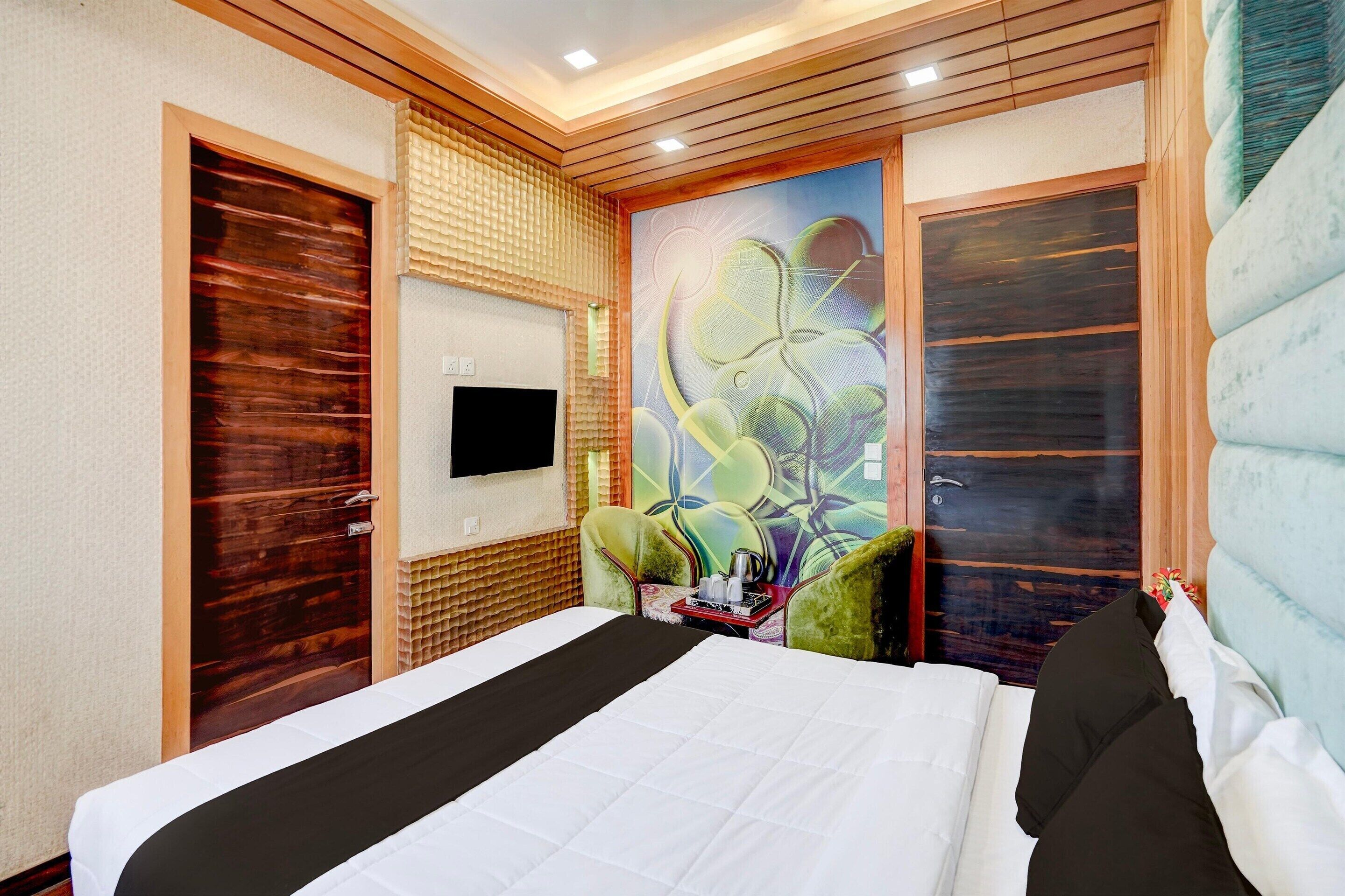 Habitación de hotel con cama, televisión de pantalla plana en la pared y un mural decorativo.