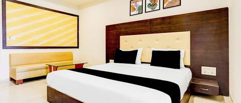 A modern bedroom with a large bed, a sofa, a ceiling fan, and framed artwork on the wall.