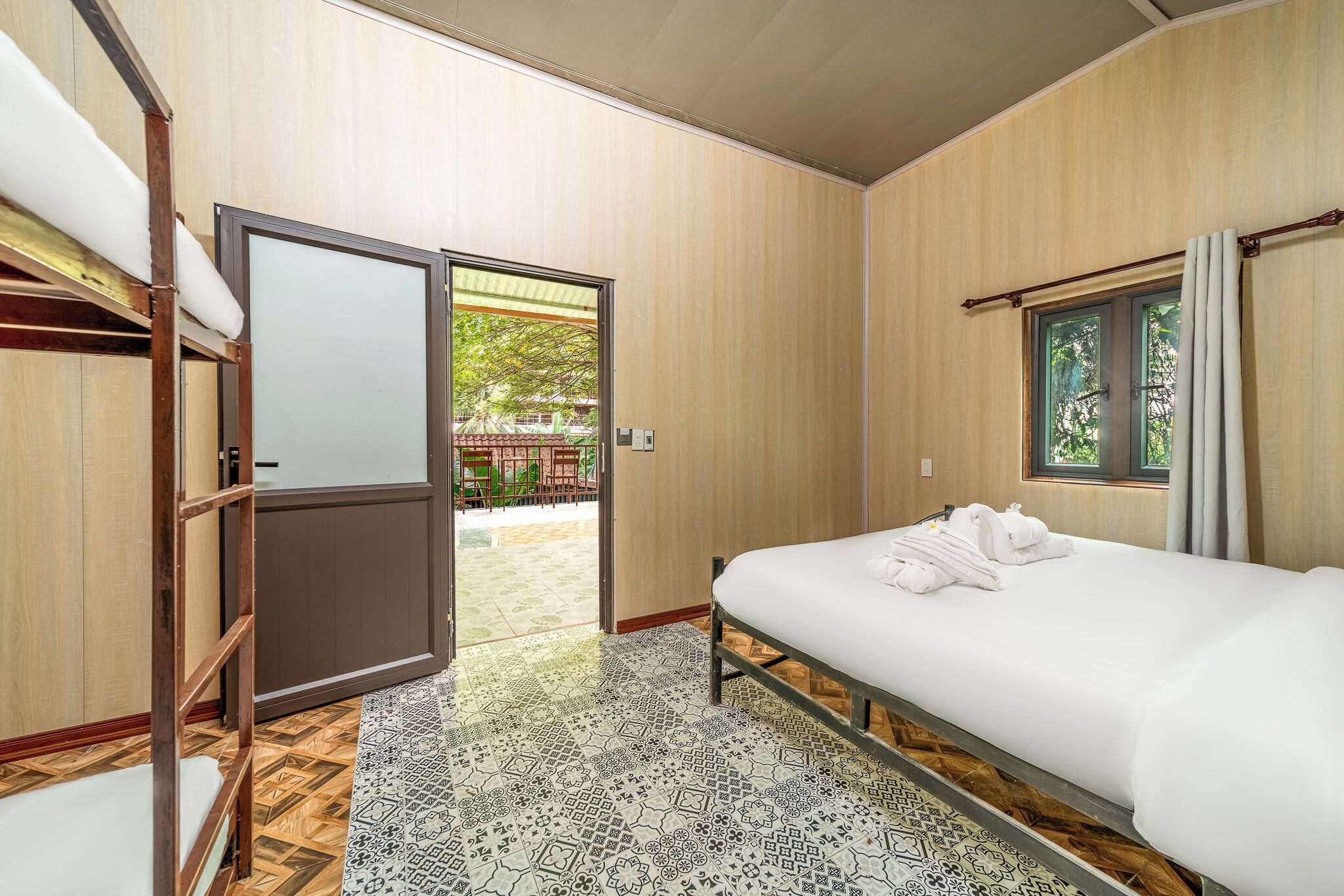 Una habitación de hotel con cama, armario de madera, ventana con cortinas y vistas a un área exterior.