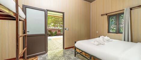 A hotel room with a bed, a wooden wardrobe, a window with curtains, and a view of an outdoor area.