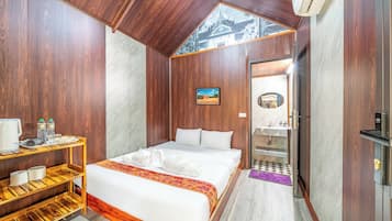 Habitación de hotel con cama, una mesita con artículos de aseo, un estante con toallas y vista a un templo a través de una ventana.