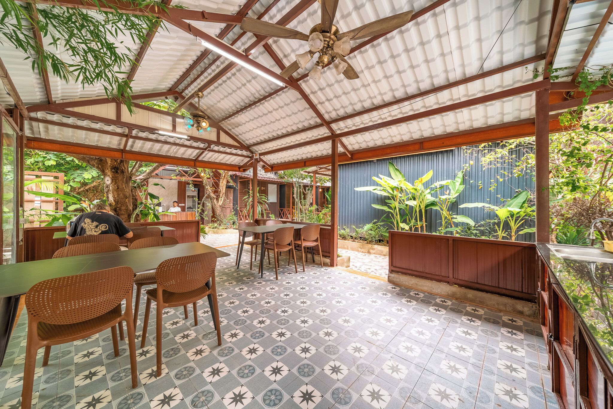 An outdoor covered patio with tables and chairs, a ceiling fan, and a view of the surrounding greenery.