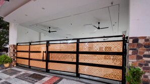 A gated entrance with a patterned screen, ceiling fans, and a stone wall. - Deluxe Gomti Nagar Station Budget In (Lucknow)