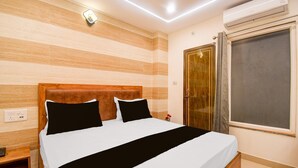 A hotel room with a wooden headboard, a bed with white and black bedding, a bedside table, an air conditioning unit, and a window with curtains. - Deluxe Gomti Nagar Station Budget In (Lucknow)