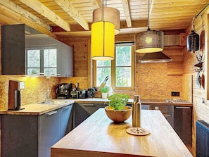 A modern kitchen with wooden beams, a central island, a coffee machine, and a window with a view of trees.