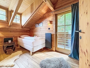 Ein Schlafzimmer in einer Holzhütte mit einem Bett, einem kleinen Tisch, einem Heizkörper und einem großen Fenster mit Vorhängen.
