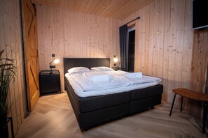 A wooden-paneled room with a bed, bedside tables, a bench, and a TV mounted on the wall. - Kleines Studio in Niedersfeld an der Skipiste (Winterberg)