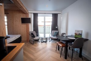 A modern room with a bed, a TV, a dining table with chairs, and a balcony with curtains. - Kleines Studio in Niedersfeld an der Skipiste (Winterberg)
