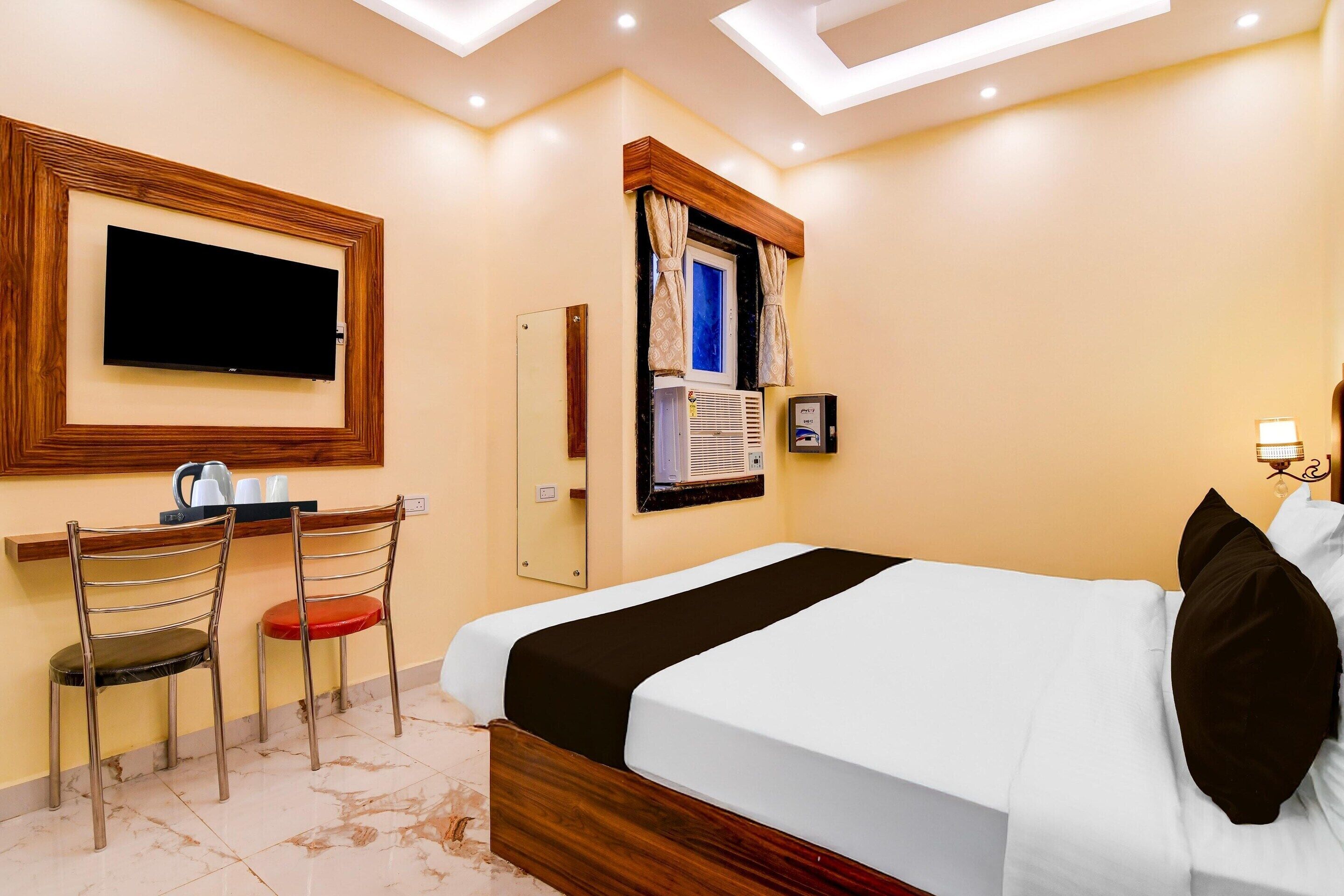 A hotel room with a bed, a TV mounted on the wall, a desk with chairs, and a window with curtains.