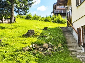 Ein Hang mit einer Steinmauer, einer Treppe, die zu einem Gebäude mit einem Balkon führt, und einem Baum.