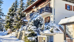Un edificio de varios pisos con un balcón, rodeado de árboles cubiertos de nieve y un cielo despejado.