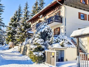 Ein mehrstöckiges Gebäude mit Balkon, umgeben von schneebedeckten Bäumen und blauem Himmel.