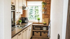 Una cocina compacta con armarios de madera, cafetera, lavamanos y ventana con plantas.