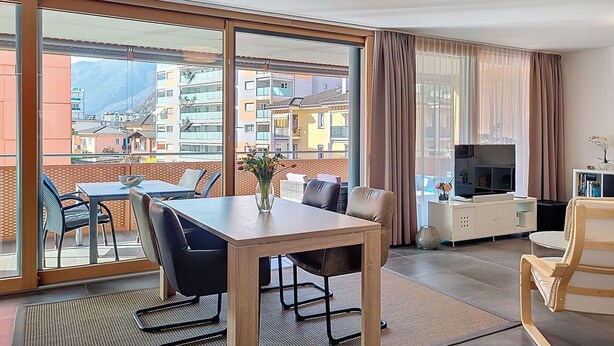 Un soggiorno moderno con zona pranzo, ampie porte scorrevoli in vetro e vista sulla città.