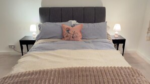 A bed with a headboard, two bedside tables with lamps, and a patterned throw blanket. - Stylish apartment in city centre, excellent link to London by rail, bus & road (Camberley)
