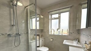 A bathroom with a glass shower enclosure, a toilet, a sink, and a window. - Stylish apartment in city centre, excellent link to London by rail, bus & road (Camberley)
