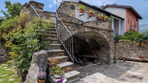 Una scala in pietra conduce a un balcone con piante in vaso, una bicicletta e un muro di pietra rustica.