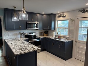 A modern kitchen with dark cabinetry, a stainless steel microwave, a double oven, and a granite countertop. - 4-bedroom house in Holden Beach with Beach Access directly across the street! (Holden Beach)