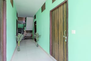 A hallway with a green wall, a wooden door, and two potted plants.
