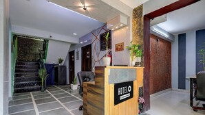 A hotel reception area with a reception desk, a staircase, and a potted plant. - Super Hotel O Dadri Main Greater Noida (Greater Noida)