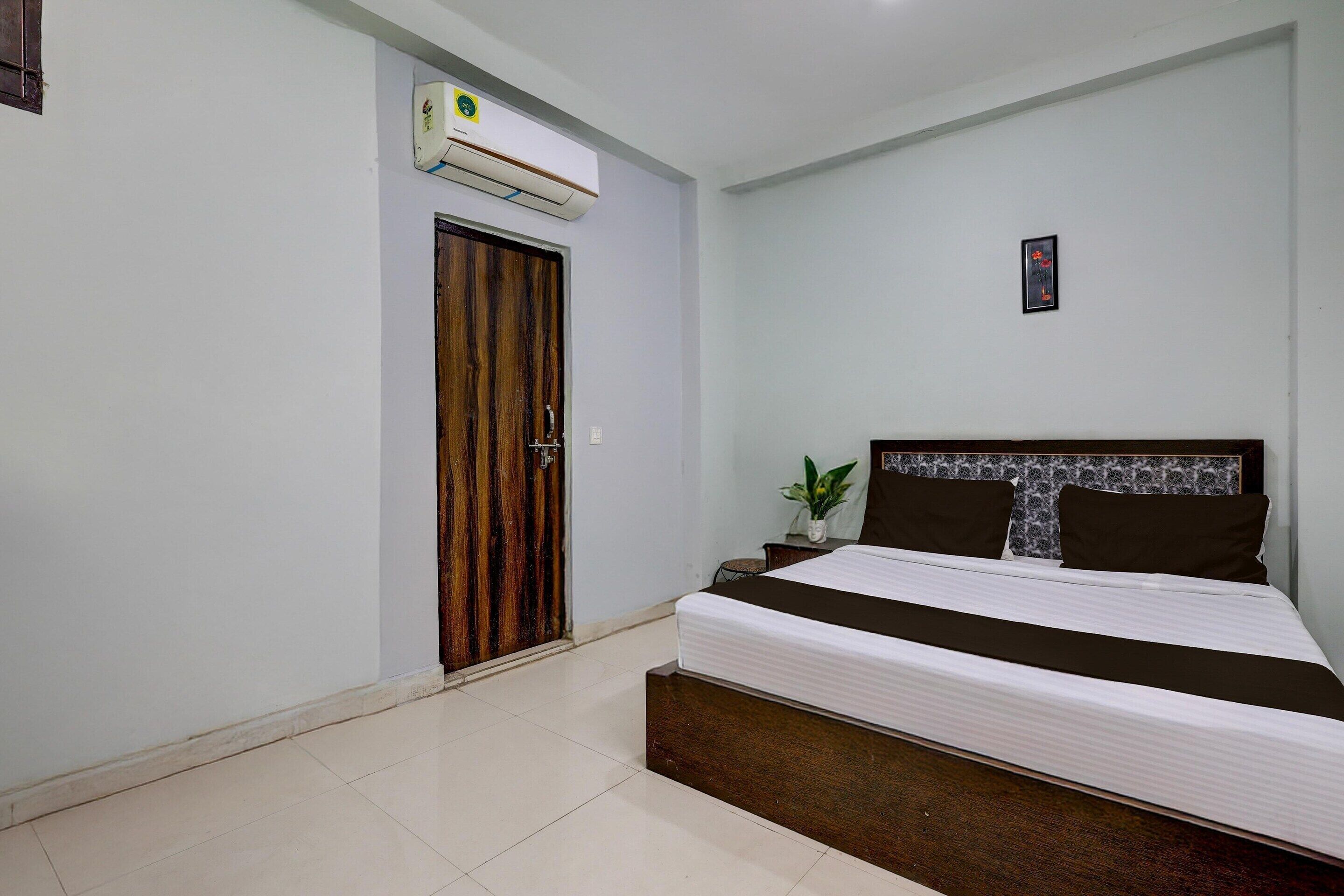 Un dormitorio con una cama, una puerta de madera, aire acondicionado y una planta pequeña.