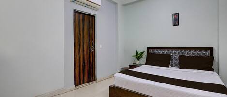 Un dormitorio con una cama, una puerta de madera, aire acondicionado y una planta pequeña.
