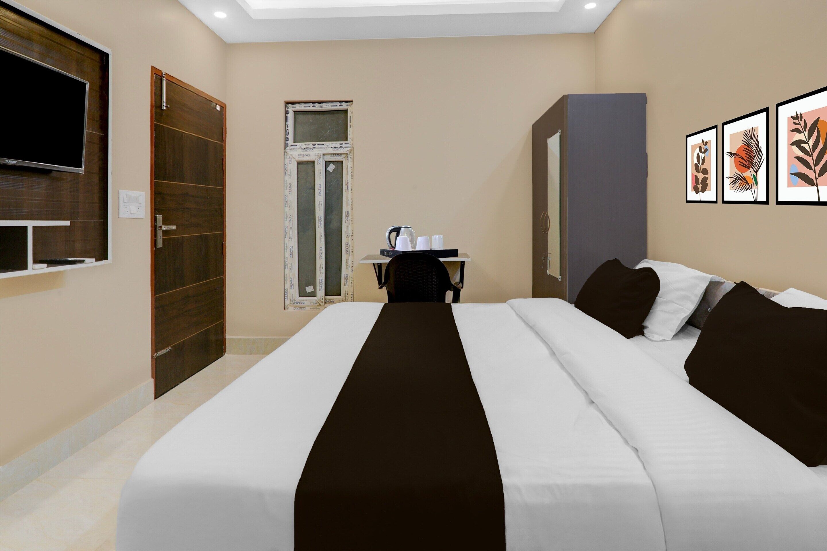 A hotel room with a large bed, a desk with a chair, a television, and framed artwork on the wall.