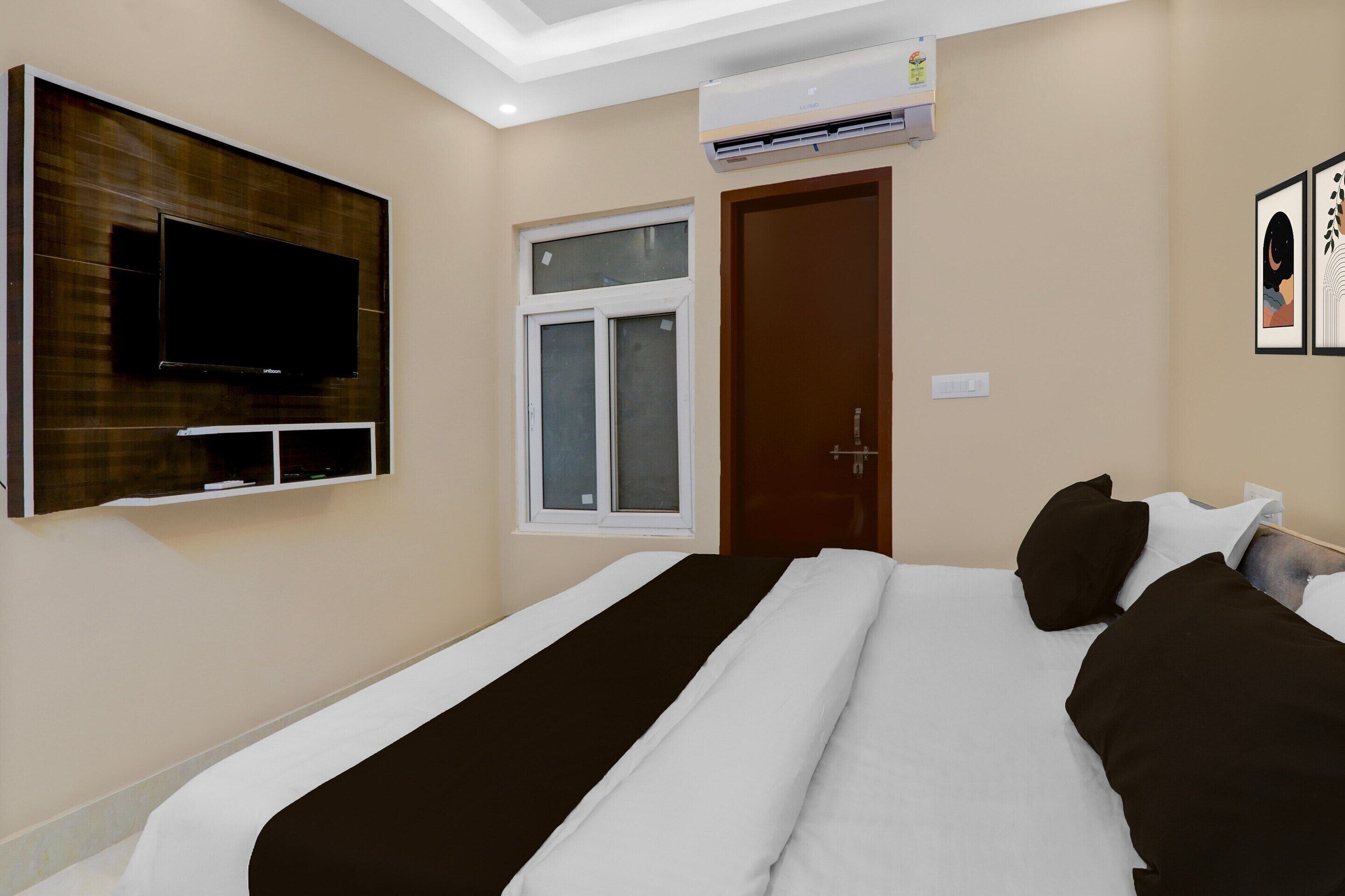 A hotel room with a bed, a TV mounted on the wall, a window, and an air conditioning unit.
