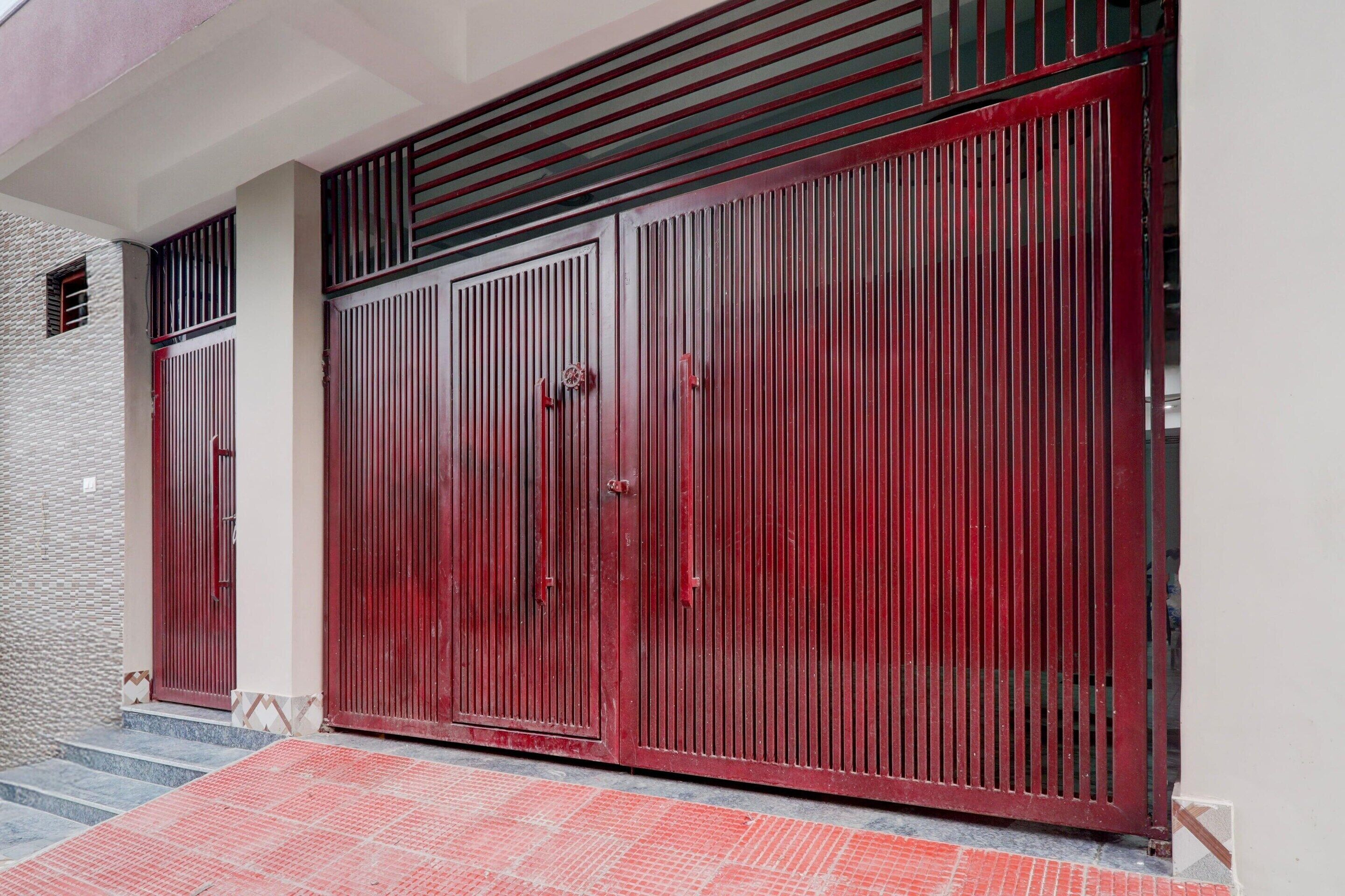 A large red metal gate with vertical bars, a small window, and a red-tiled entrance.