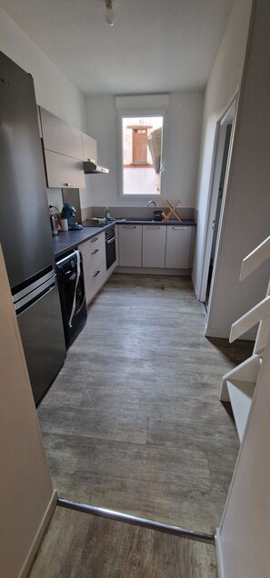Eine moderne Küche mit grauen Schränken, einem schwarzen Kühlschrank und einem Fenster, das für natürliches Licht sorgt.