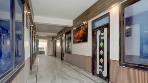 A corridor with a marble floor, glass doors, and framed artwork on the walls. - Deluxe Pushp Vatika (Varanasi)