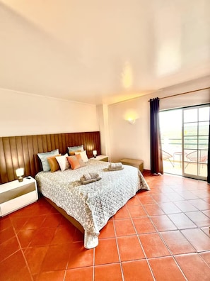 Un dormitorio con una cama grande, una mesita de noche, una lámpara de pared y vistas al exterior a través de una puerta corrediza de vidrio.