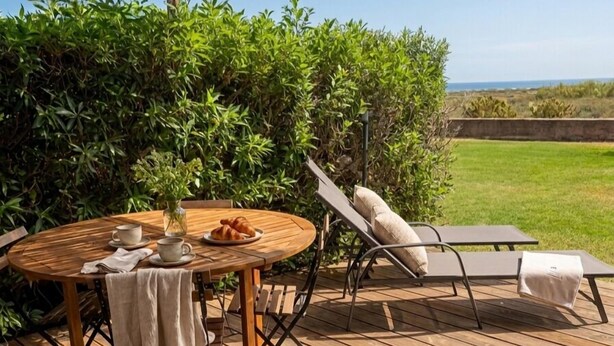 Ett trädäck med ett runt bord, två solstolar och en pergola.