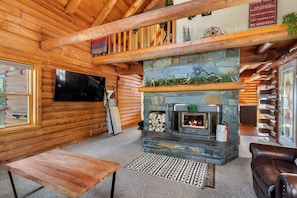 A log cabin interior with a stone fireplace, wooden walls, a television, and a leather sofa.