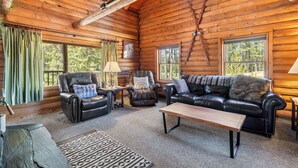 A log cabin interior with a leather sofa, armchairs, a coffee table, and a patterned rug. - Hilltop Log Cabin Retreat with Hot Tub & Direct Trail Access Near Lead (Lead)
